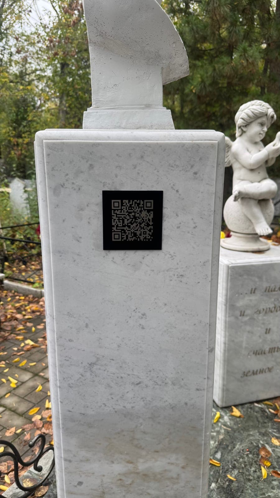 Чёрная табличка с QR‑кодом на белом постаменте с бюстом