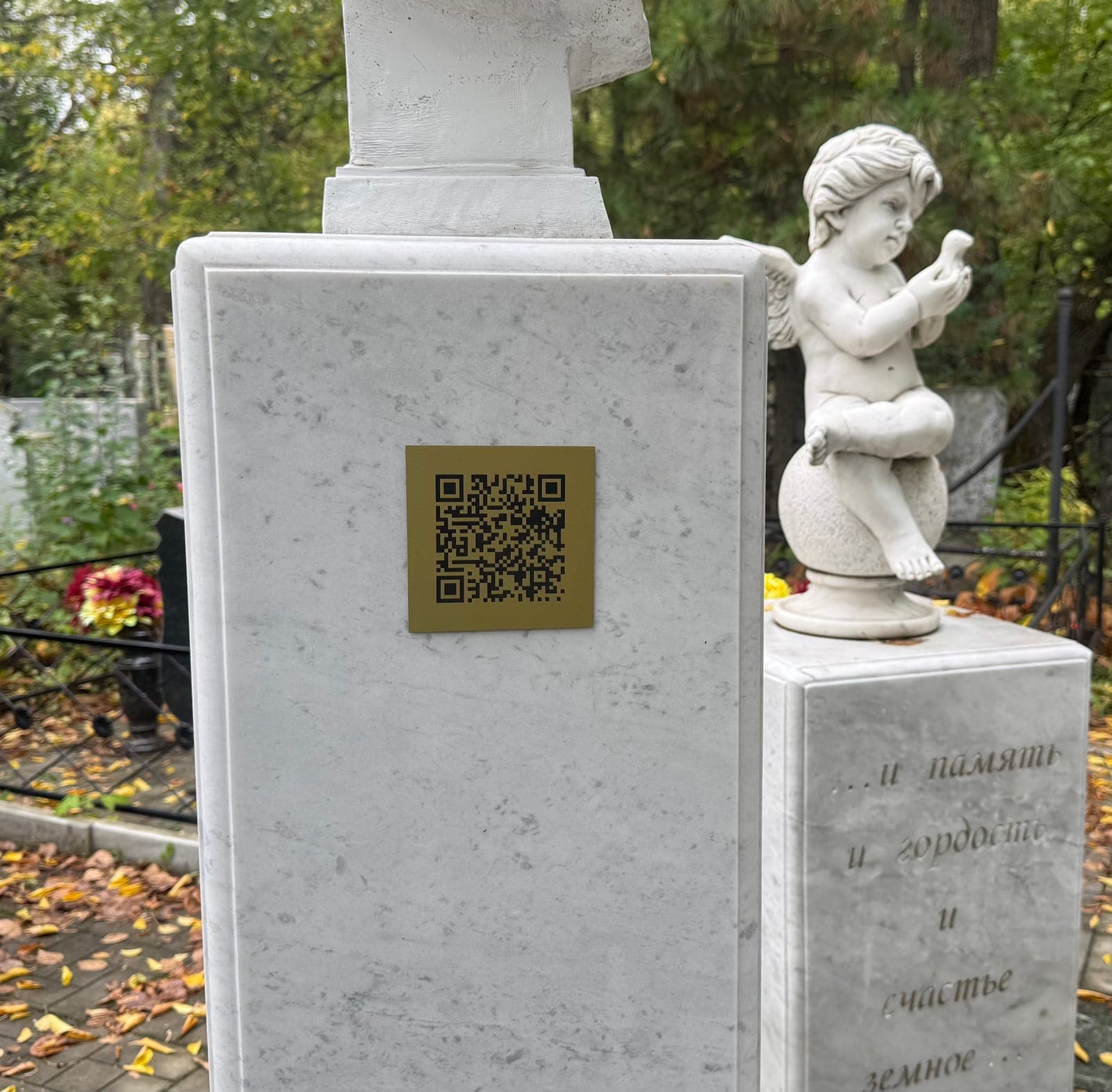 Золотистая табличка с QR‑кодом на мраморном памятнике с ангелом