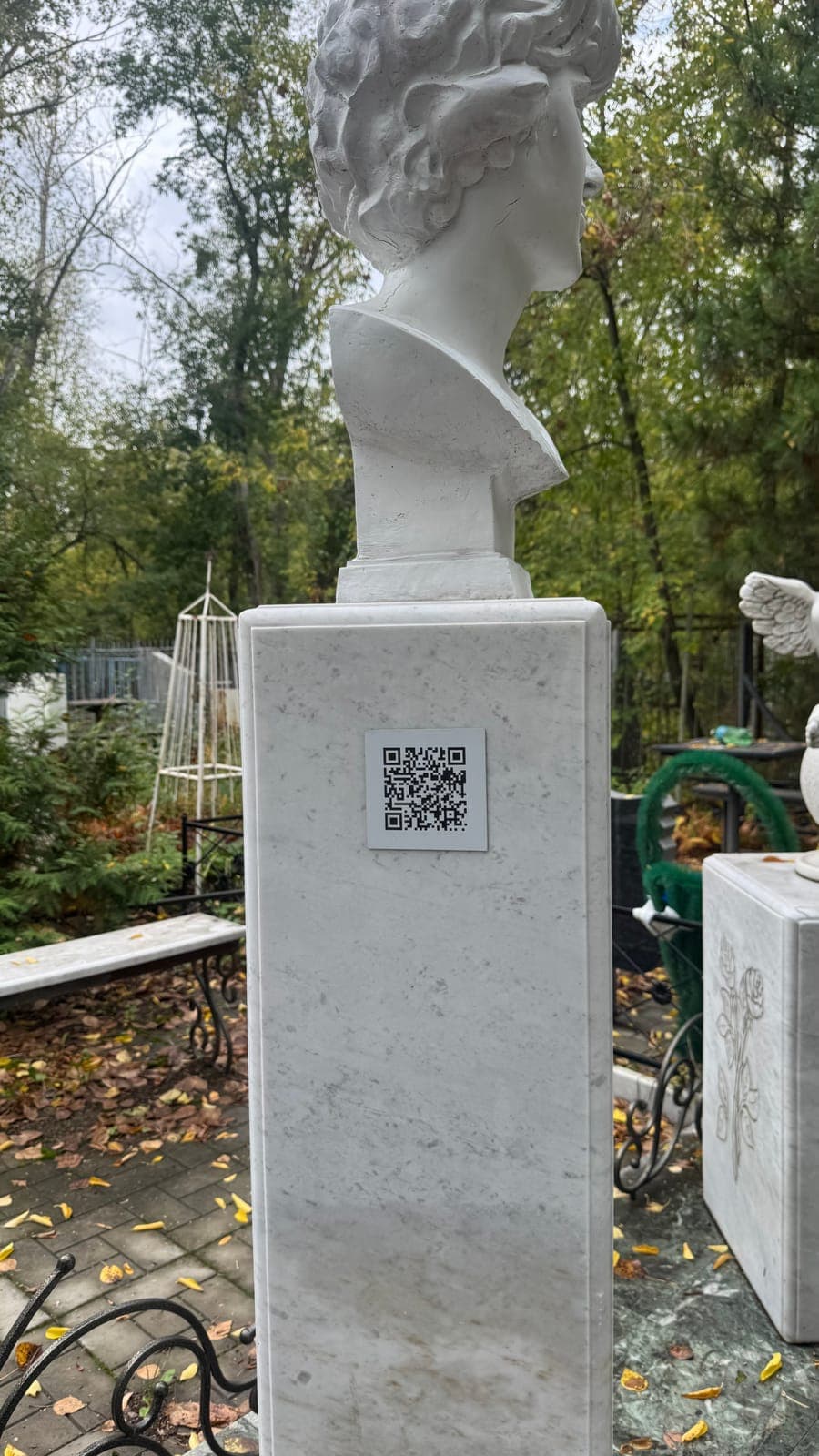 Белая табличка с QR‑кодом на мраморном постаменте с бюстом